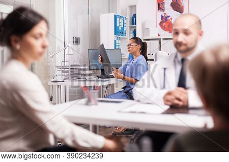Nurse In Blue Uniform Holding X-ray Image In Hospital Office While Doctor Is Consulting Disabled Sen