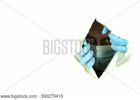 A Man In A Mask And Gloves Looks Through The Hole. Situation A Man In A Medical Mask Peeps Through A