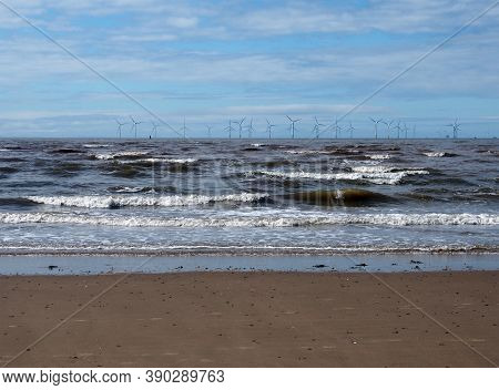 The Beach At Blundell Sands In Southport With Waves Braking On The Beach And The Wind Turbines At Bu
