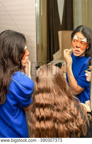 Young Girl For Masquerade Paints Her Face With Paints Standing In Front Of A Mirror