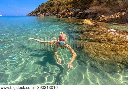 Italian Girl Swims In Fetovaia Beach Sea Wearing Medical Mask During Covid-19. Blonde Woman Having A