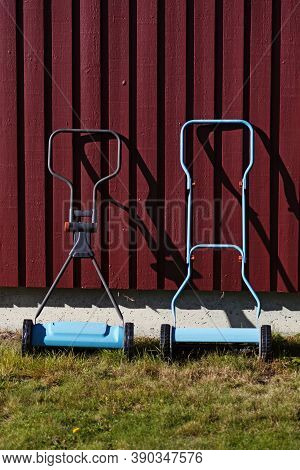 Two Light Blue Lawnmowers Against Red Wooden Wall