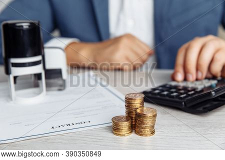 Businessman Approves Important Contract. Stack Of Coins And Stamps On Desk. Business Concept