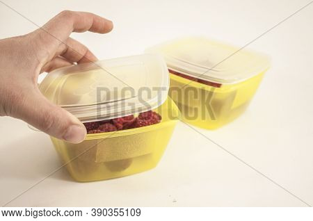 A Woman's Hand Closes The Lunchbox, The Photo Shows A Hand And Two Yellow Lunchboxes With Raspberrie