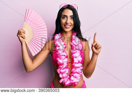 Beautiful hispanic woman wearing bikini holding handfan smiling with an idea or question pointing finger with happy face, number one 