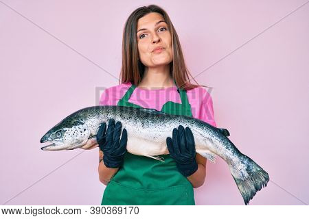 Beautiful caucasian woman fishmonger selling fresh raw salmon looking at the camera blowing a kiss being lovely and sexy. love expression. 