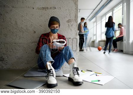 Young Student With Face Mask Sitting On Floor Back At College Or University, Coronavirus Concept.