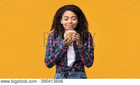 Delicious Meal. Portrait Of Hungry Black Female Model Eating Burger. Smiling African American Woman 
