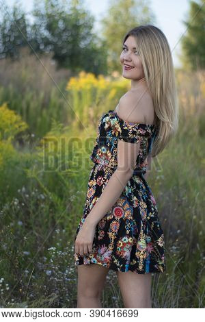 Overlight Bright Portrait Of A Charming Attractive Blonde In Flowery Dress In The Field