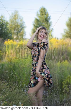 Overlight Bright Portrait Of A Charming Attractive Blonde In Flowery Dress In The Field