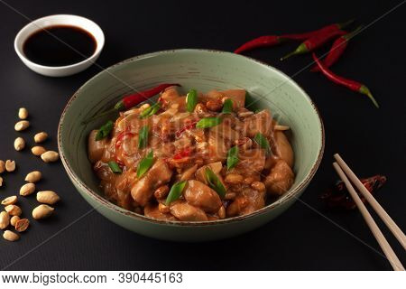 Kung Bao Chicken On A Black Background. A Chinese Dish With Chicken, Chili, Peanuts, Sauces And Onio