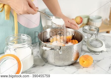 Woman Adding Sugar Into Pot With Apricots At Table In Kitchen, Closeup. Making Delicious Jam