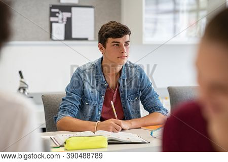 Young college student listening carefully while in lecture. University young man studying and writing in book while in class. Intelligent high school student with open book in class studying.