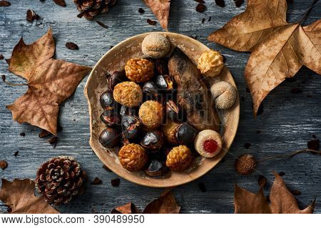 high angle view of a plate with some roasted sweet potato, some roasted chestnuts and some panellets, typical confection of Catalonia, Spain, eaten traditionally in All Saints Day, on a rustic table