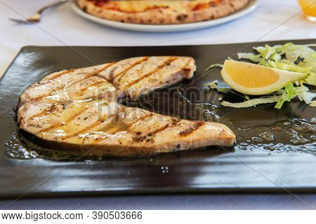Cooked swordfish. Grilled slice of fish with lemon and salsd on plate in restaurant