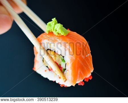 Man Holding Wooden Chopsticks Sushin, On Top Of Wasabi Sushi. Dark Background.