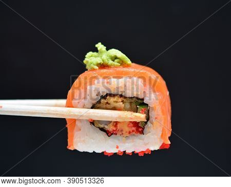 Man Holding Wooden Chopsticks Sushin, On Top Of Wasabi Sushi. Dark Background.