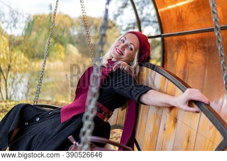 The Girl On The Swing On The Pond Is Brown, In A Red Biret And Scarf, In A Black Pal Autumn Happy Si