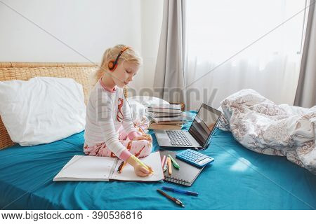 Caucasian Girl Child Sitting In Bed And Learning Online On Laptop Internet. Virtual Class Lesson On 