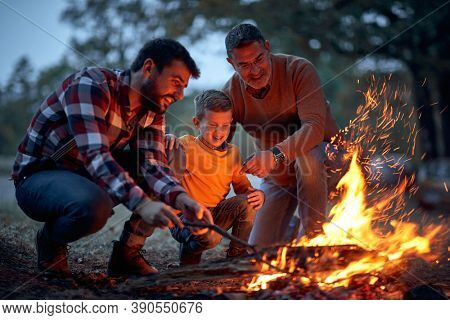 Father, son and grandson lit up a campfire in the forest on a beautiful autumn dusk