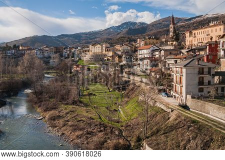 Dronero Town And River With Snow On The Mountains Scenic View In Cuneo Province, Piedmont, Italy