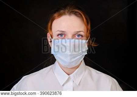 A Woman With Red Eyes In A White Shirt And A Medical Mask On A Black Background. People Caught In Is