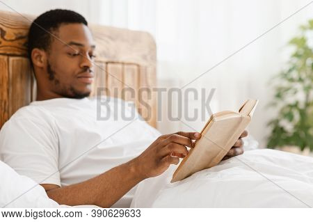 African American Man Reading Books Enjoying Weekend Morning Sitting In Bed In Bedroom At Home, Focus