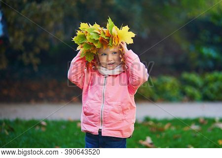 Adorable Toddler Girl In Beautiful Wreath Made From Fallen Maple Leaves In Autumn Park. Happy Kid En