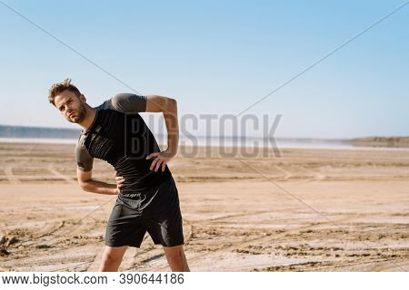 Motivated focused young sportsman exercising at the beach, stetching