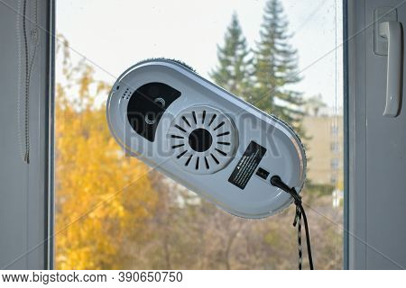 Robot For Cleaning Windows And Ceramic Tiles Against A Background Of A Window And An Autumn Landscap