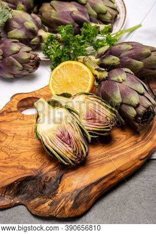 Fresh French Petit Violet Artichokes Heads Cultivted In Brittany, France With Lemon And Parsley