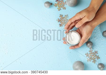 Female Hands Hold Cosmetic Cream On Blue Background With Baubles