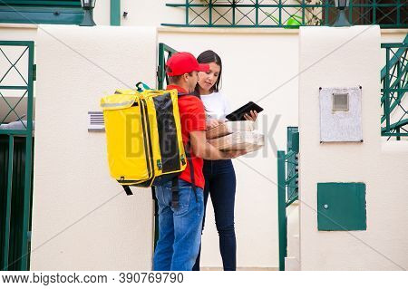Serious Deliveryman Holding Parcels And Woman Checking Order. Content Courier In Red Cap And Shirt W