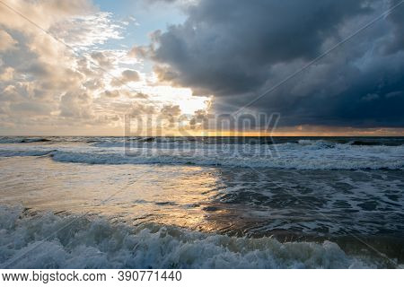 Sunset On The North Sea Near The Town Of Petten, With Dark Colored Clouds And An Orange Setting Sun