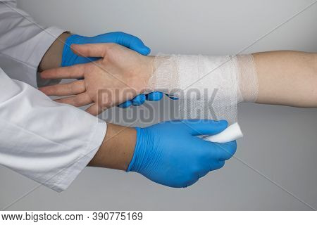 The Traumatologist Puts A Bandage On The Forearm Of The Female Patient. The Concept Of Help With Fra