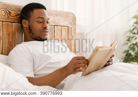 Black Man Enjoying Reading Book In The Morning Lying In Comfortable Bed At Home. Bookworm Guy Reads 