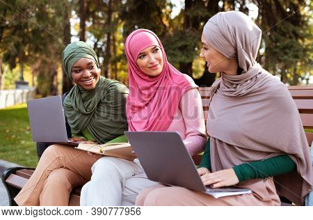 Three Modern Isamic Ladies With Laptops And Books Learning Together Talking Sitting On Bench In Park