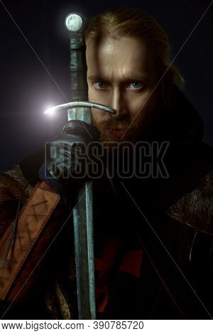 Portrait of a medieval knight in armour and with a sword over black background. Knight Templar. Historical reenactment.