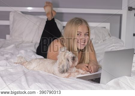 Beautiful Blonde With A Puppy Shih-tzu And Laptop On Bed With White Sheets. Pretty People And Pets O