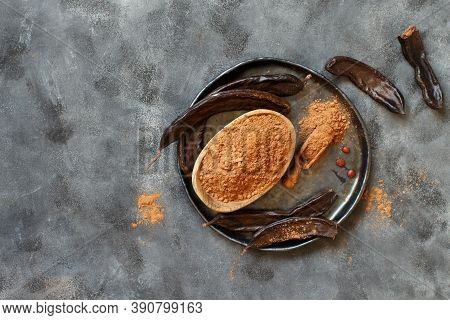 Dry Carob Powder And Pods Top View On A Grey Table