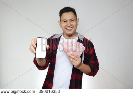 Happy Cheerful Asian Man Holding Uang Indonesian Rupiah Money And Showing Phone With Empty Blank Scr