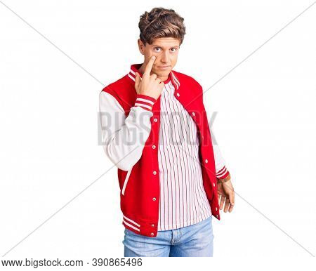 Young handsome man wearing baseball uniform pointing to the eye watching you gesture, suspicious expression 