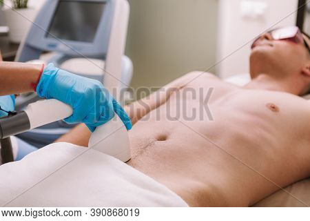 Beautician Removing Pubic Hair Of A Male Client With Laser. Man Getting Laser Hair Removal Treatment
