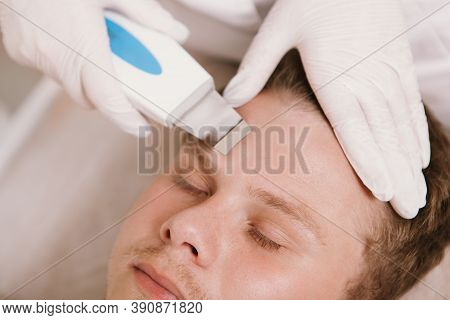 Cropped Close Up Of A Dermatologist Using Ultrasound Cleaning Device On Forehead Of A Male Client