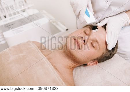 Handsome Man Getting Ultrasound Facial Cleaning Treatment By Cosmetologist