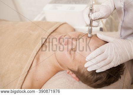 Professional Cosmetologist Tightening Skin Of A Male Client With Ultrasonic Device
