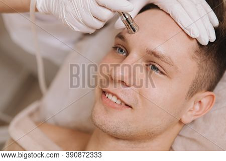 Handsome Happy Man Enjoying Facial Skincare Treatment By Cosmetologist