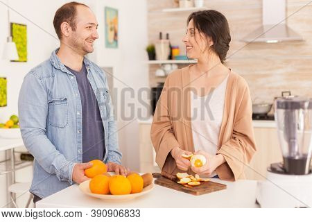 Couple Smiling At Each Other While Preparing Nutritious Smoothie. Woman Peeling Off Orange. Healthy 