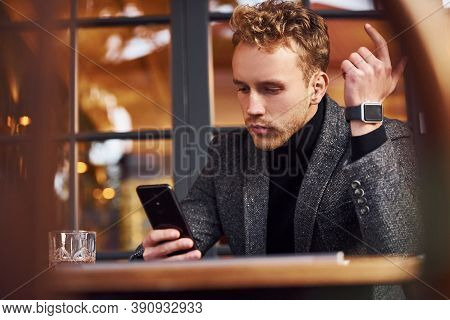 Portrait Of Modern Young Guy In Formal Clothes That Sits In The Cafe With Phone In Hands.