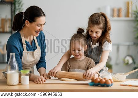 Happy loving family are preparing bakery together. Mother and children daughters girls are cooking cookies and having fun in the kitchen. Homemade food and little helper. 